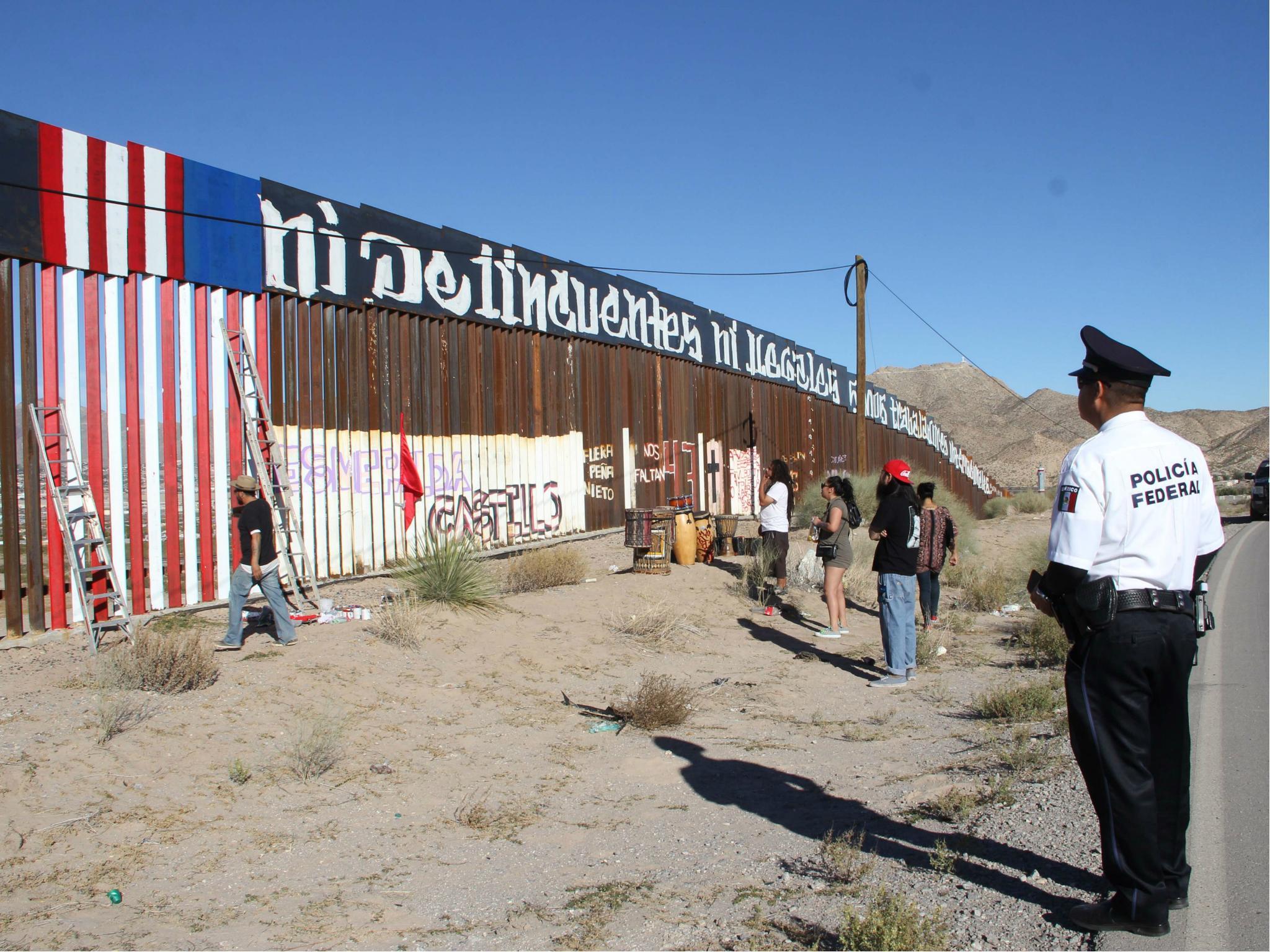 A Mexican policeman observes activists painting the border wall between the cities of Ciudad Juarez and Sunland Park