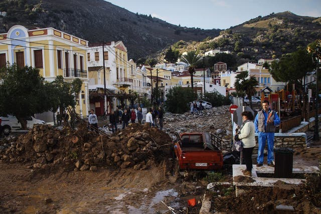 Residents stand next to a damaged road as a washed up vehicle is seen in the background following a powerful storm on the Greek island of Symi
