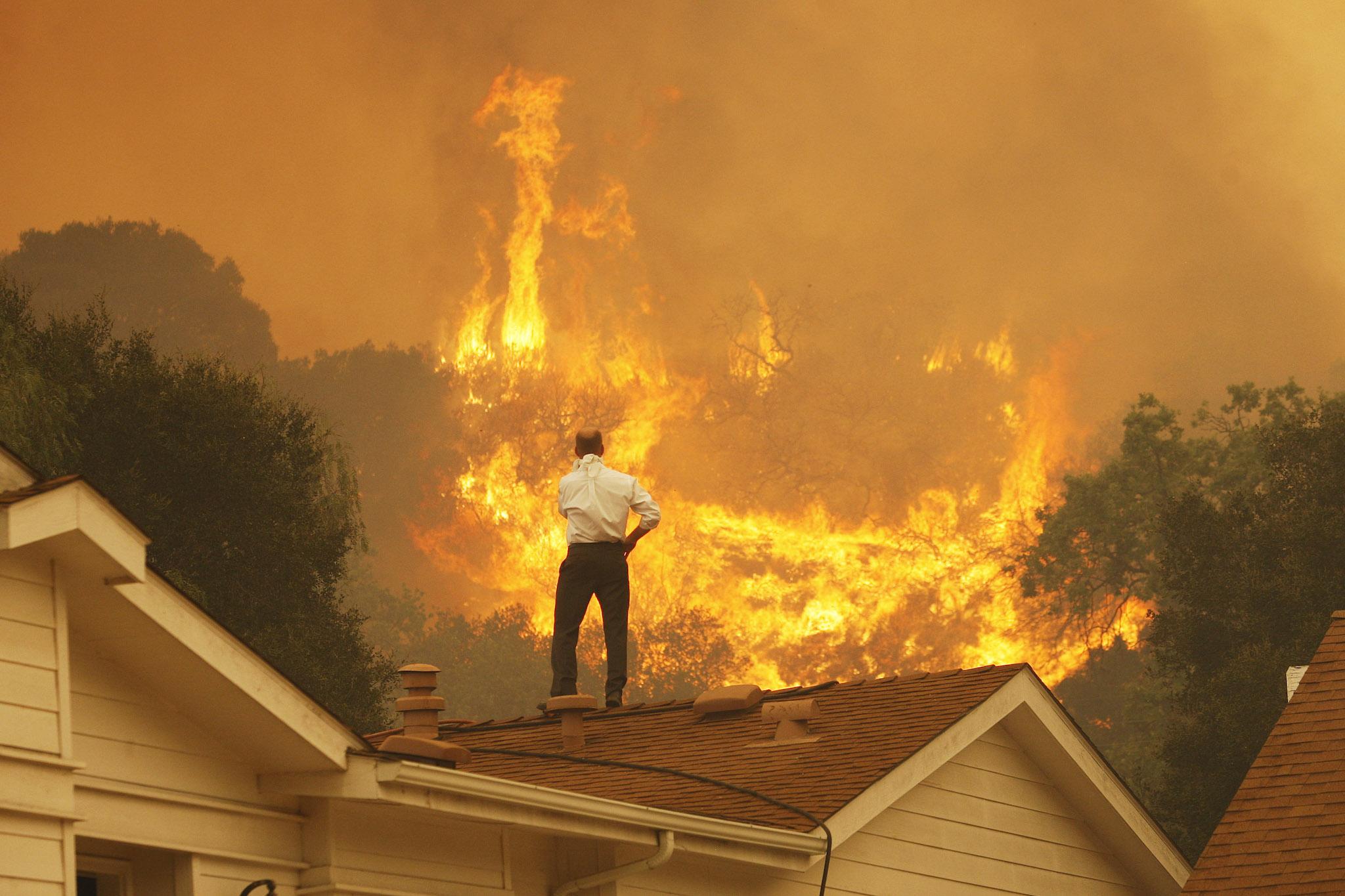 A man on a rooftop looks at approaching flames as the Springs fire continues to grow on May 3, 2013 near Camarillo, California