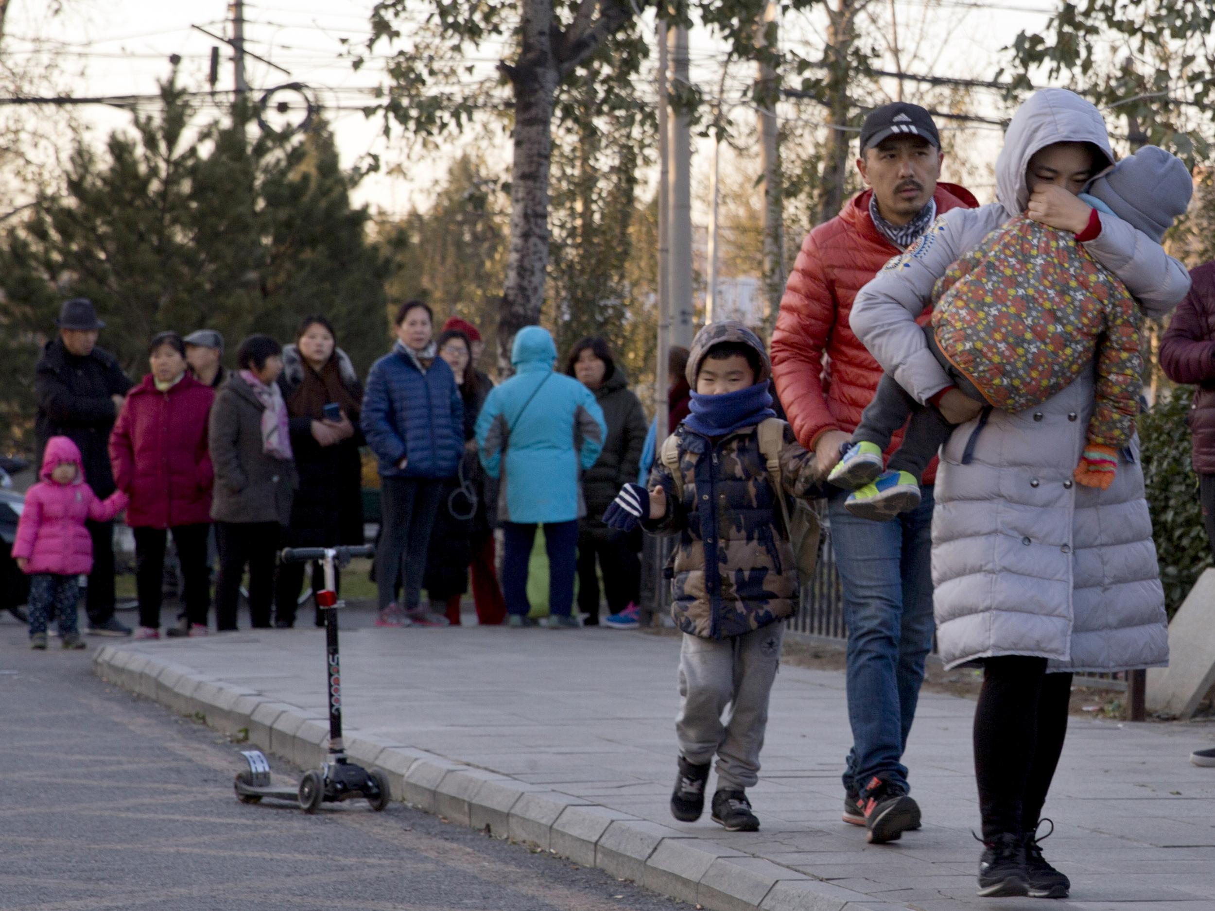 A woman carries a child as they arrive at the RYB kindergarten in Beijing