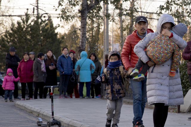 A woman carries a child as they arrive at the RYB kindergarten in Beijing