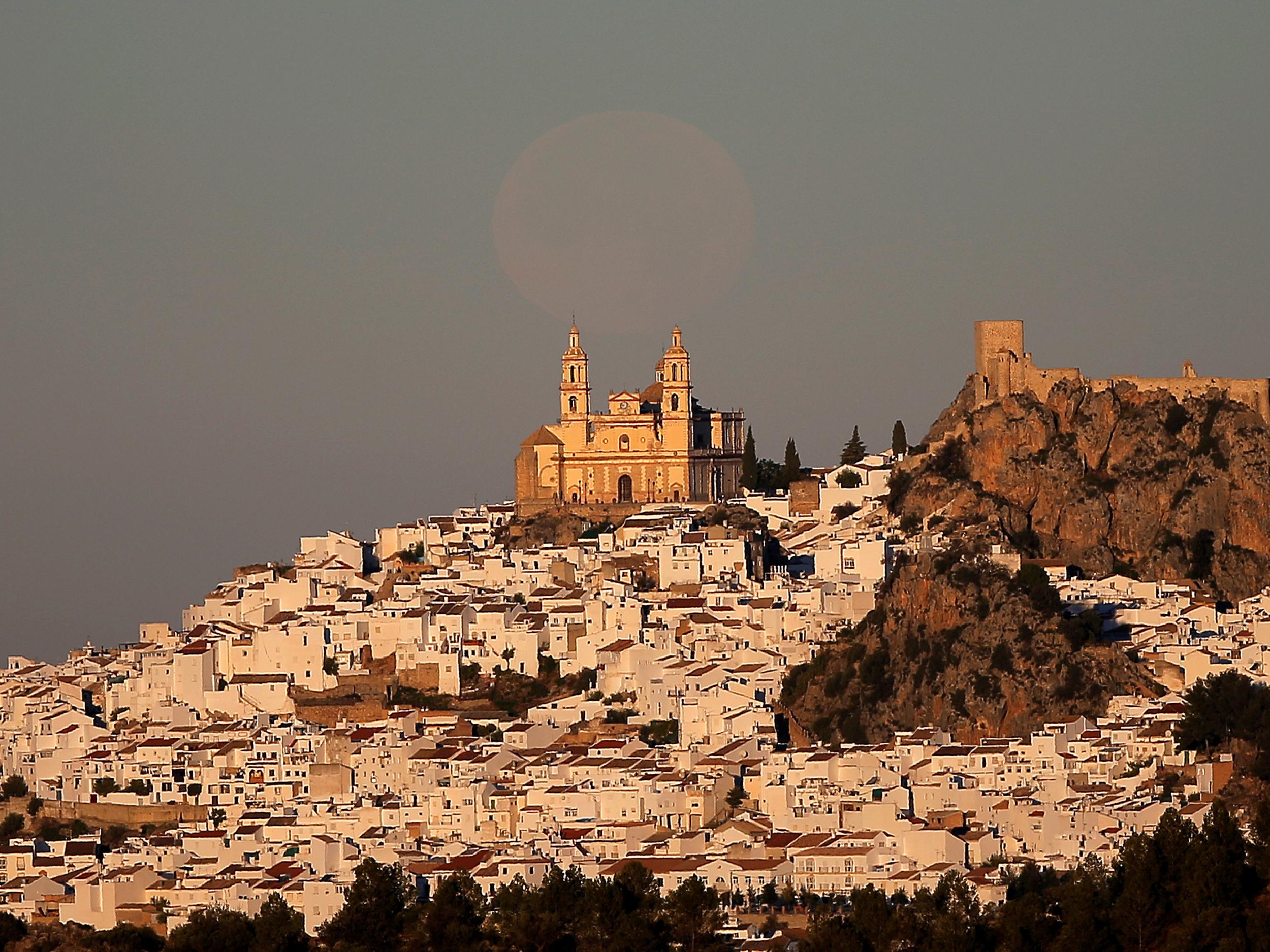 The supermoon sets over the church of Nuestra Senora de la Encarnacion at dawn in Olvera, near Cadiz, southern Spain