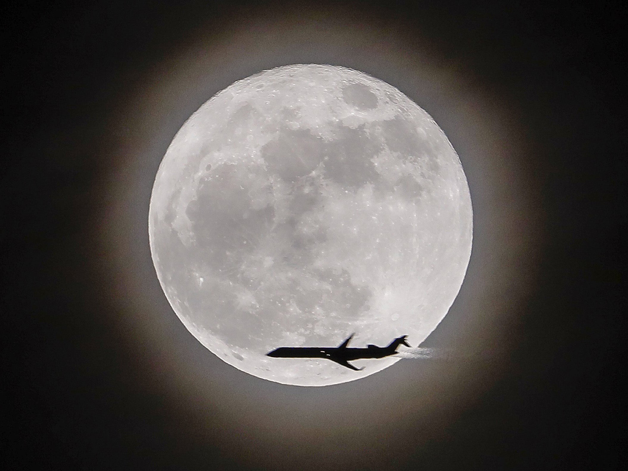 An airplane crosses in front of the supermoon, in Avondale Estates, Georgia, USA