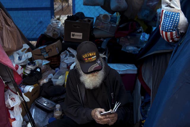 Theodore Neubauer, a 78-year-old Vietnam War veteran, who is homeless, looks at his smartphone while passing time in his tent in Los Angeles