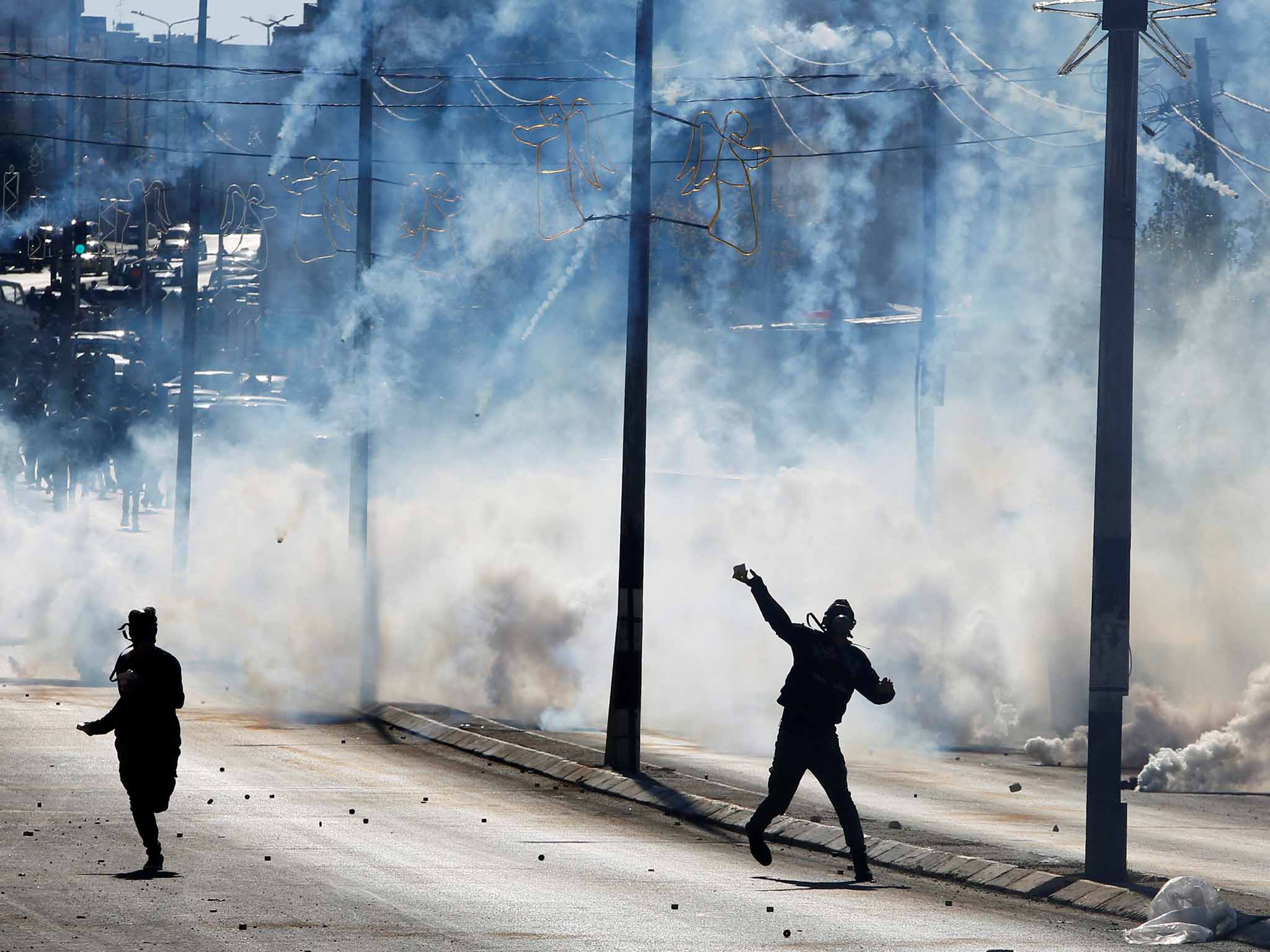 A Palestinian protester yesterday hurls stones as tear gas is fired by Israeli troops
