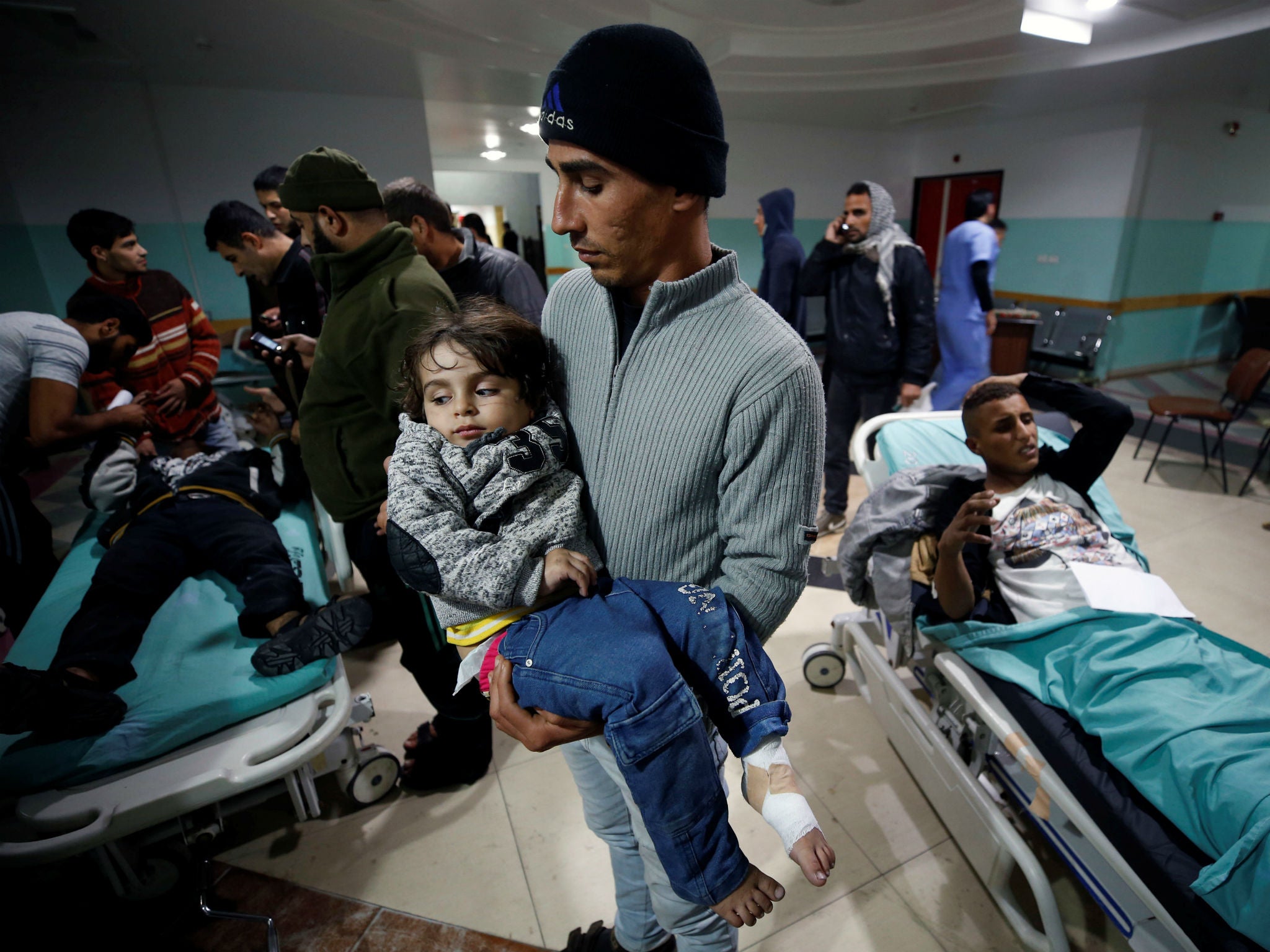 A Palestinian man carries his wounded daughter as she waits to receive treatment at a hospital near to the site of an Israeli air strike