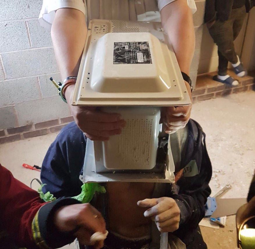 Jimmy Swingler with his head stuck in a microwave as firefighters attempt to remove it