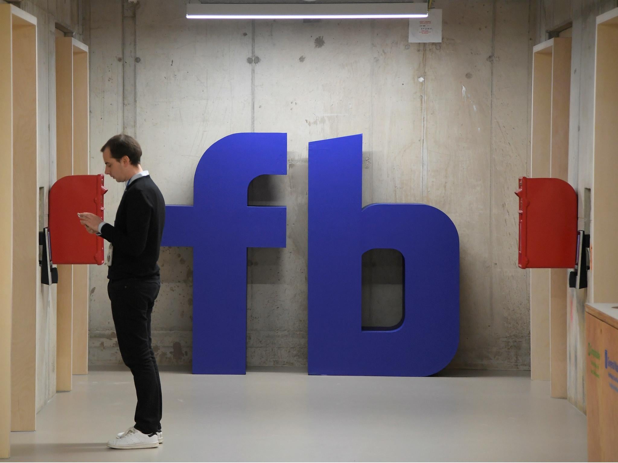 A man waits for an elevator in front of a logo at Facebook's headquarters in London, Britain, December 4, 2017