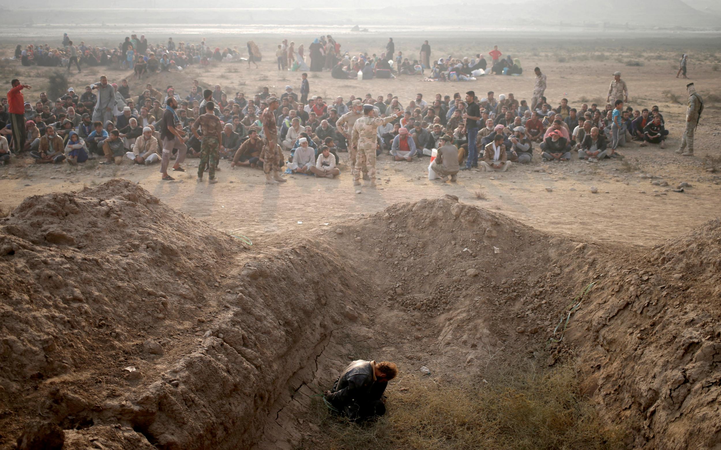 A detained man, accused of being an Isis fighter, sits in front of newly-displaced men near a check point in Qayyara, east of Mosul, Iraq, on 26 October 2016