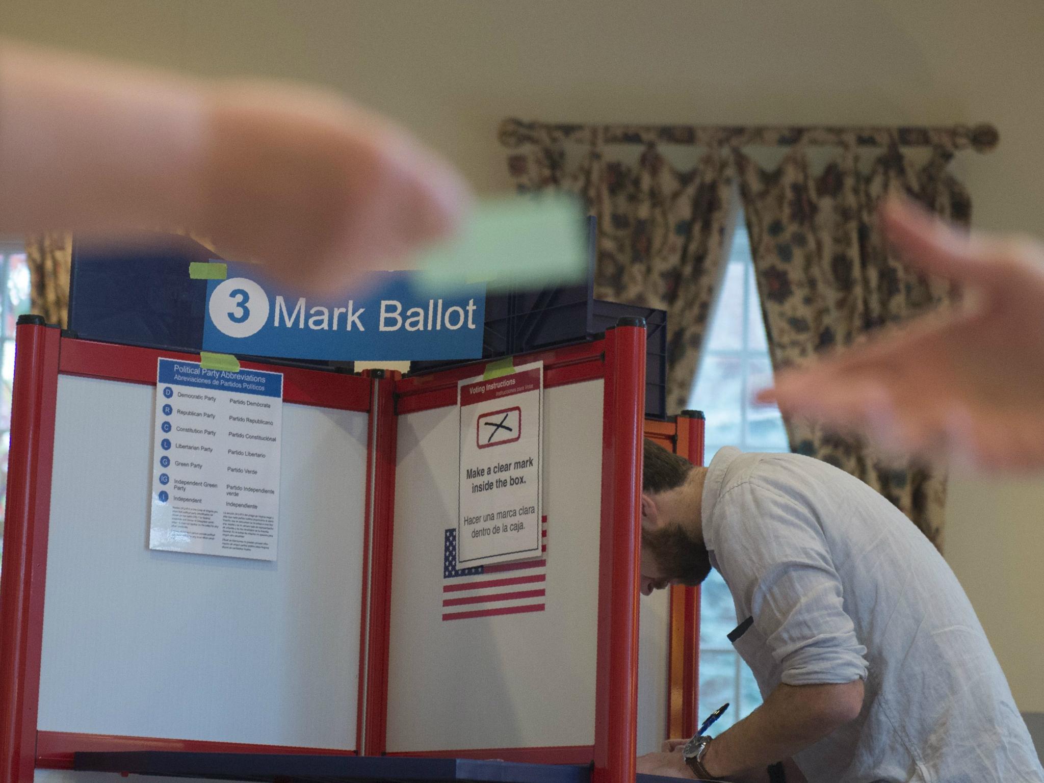 A voter hands over a card to get a ballot as someone votes in the background at a polling station in Arlington, Virginia on 7 November 2017.