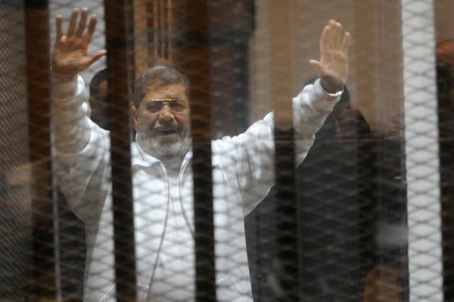 Egypt's deposed Islamist president Mohamed Morsi waves from inside the defendants cage during his trial at the police academy in Cairo on January 8, 2015.