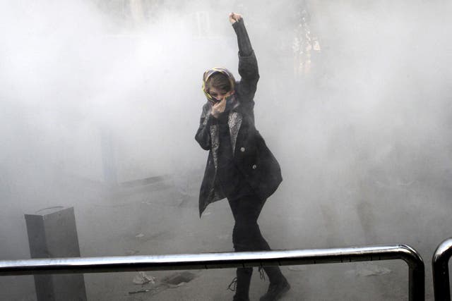 A university student attends a protest inside Tehran University while a smoke grenade is thrown by anti-riot Iranian police, in Tehran, Iran