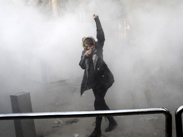 A university student attends a protest inside Tehran University while a smoke grenade is thrown by anti-riot Iranian police, in Tehran, Iran