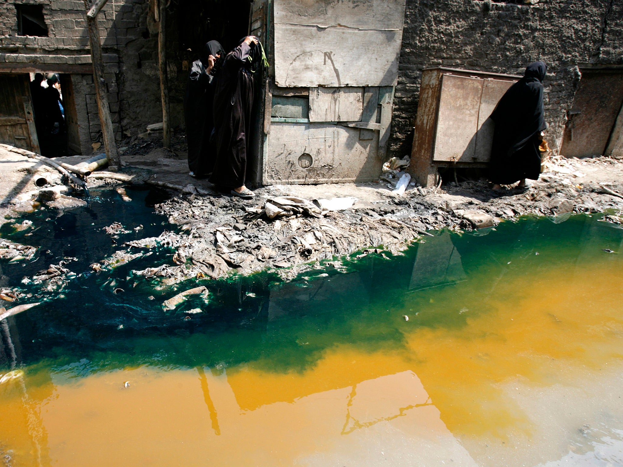 Women walk past tannery wastewater that is being pumped from a factory straight into the street, in Cairo’s Ain el Sirra district