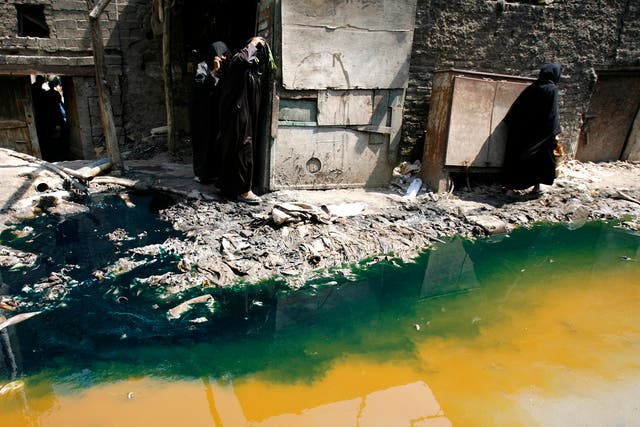 Women walk past tannery wastewater that is being pumped from a factory straight into the street, in Cairo’s Ain el-Sirra district