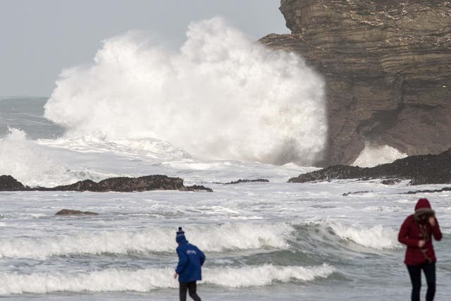 People walk on the beach as waves from stormy seas due to Storm Eleanor break behind them in Portreat, Cornwall