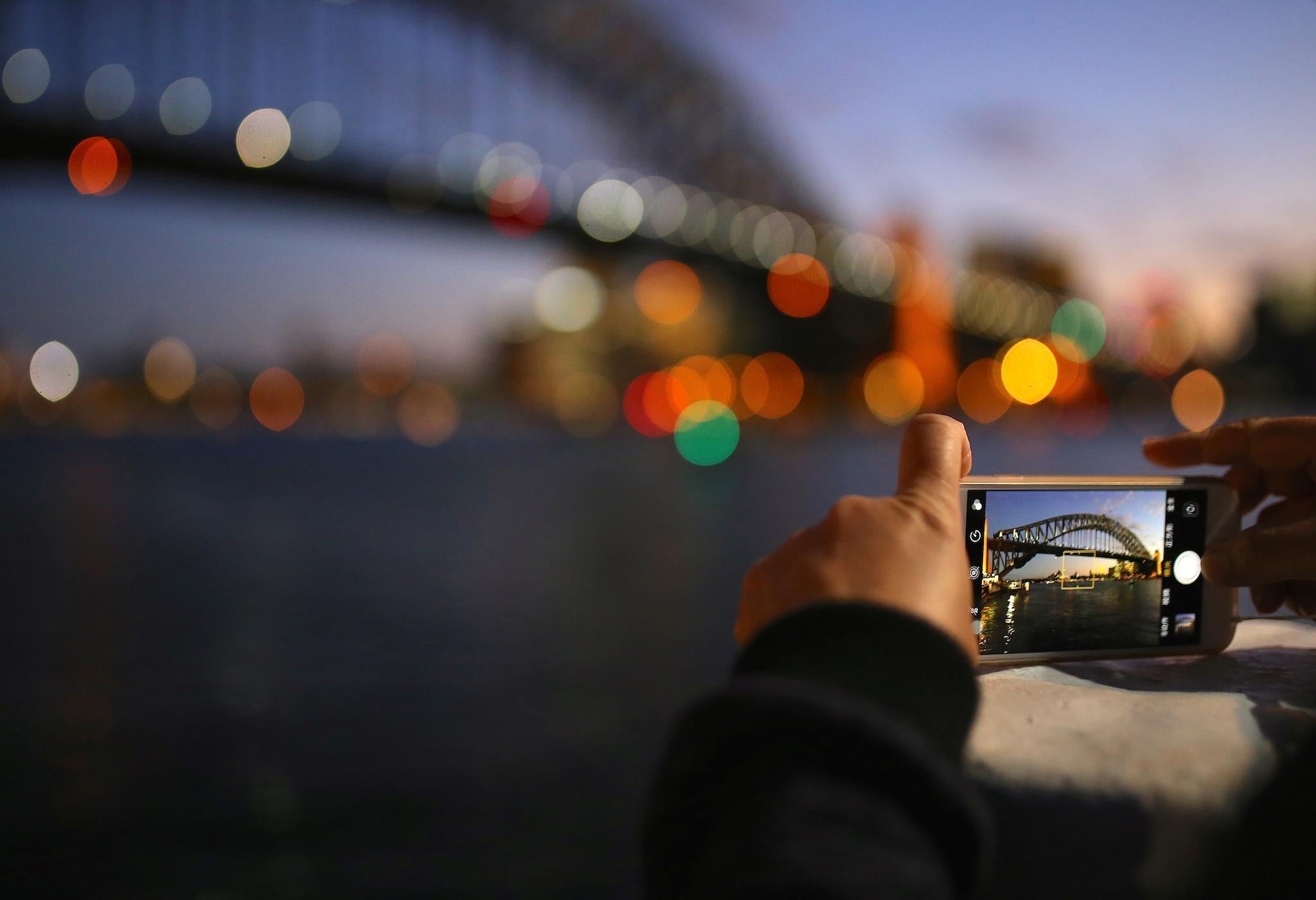 A tourist takes a photograph on their iPhone of the Sydney Harbour Bridge at sunset on a spring day in central Sydney, Australia, November 8, 2017