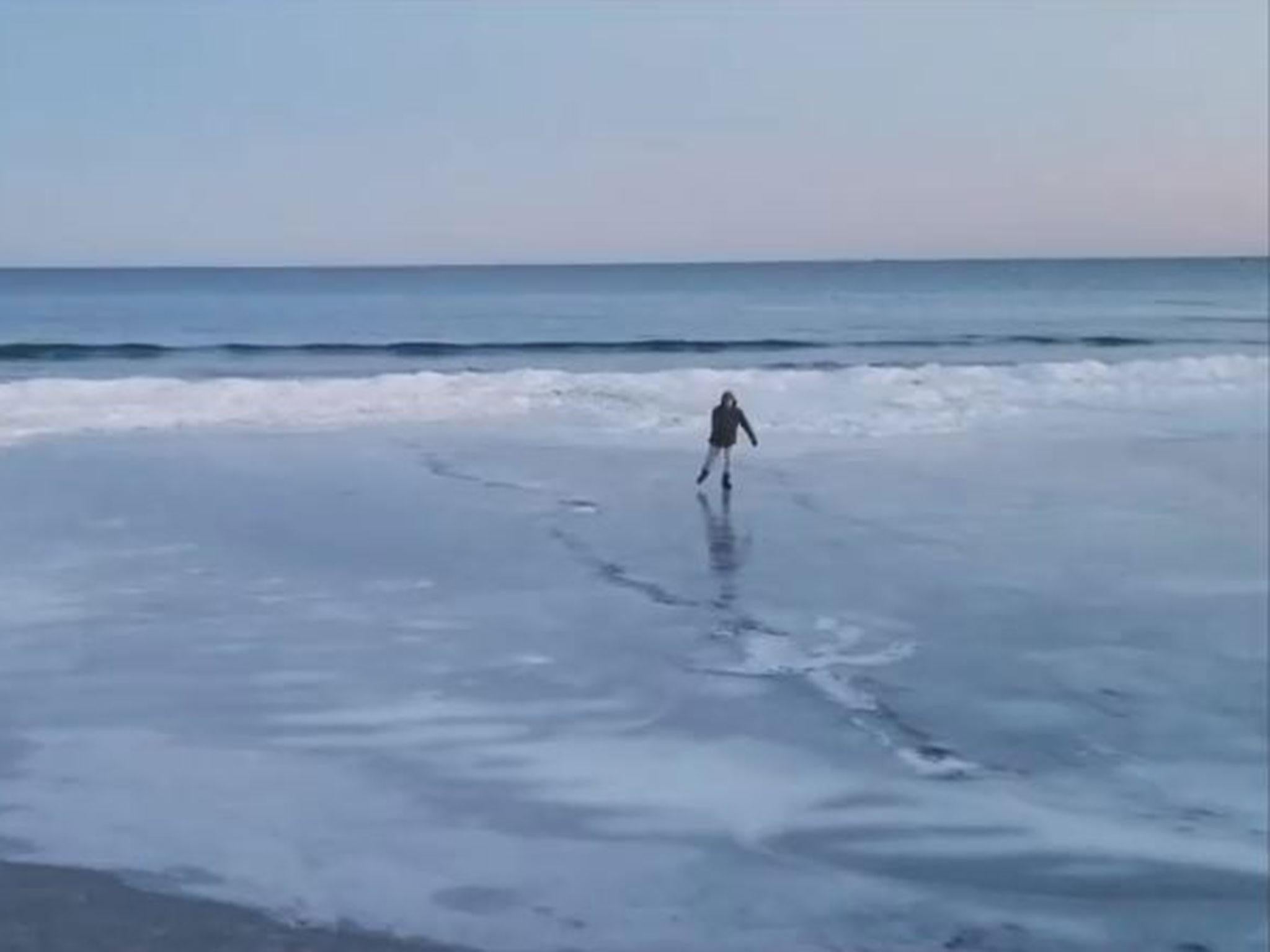A man ice-skates on a beach in Maine as families walk on the frozen sea water