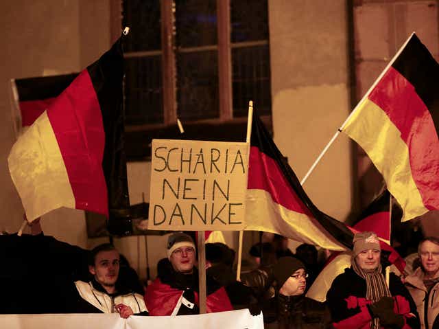 Supporters of the movement of Patriotic Europeans Against the Islamisation of the West (PEGIDA) hold German flags and a placard reading 'Sharia, no thank you.'