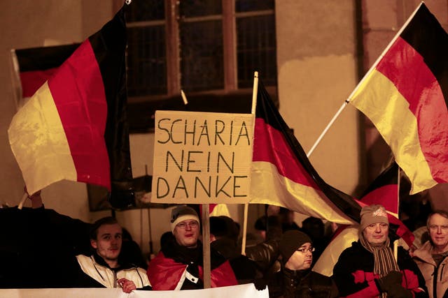 Supporters of the movement of Patriotic Europeans Against the Islamisation of the West (PEGIDA) hold German flags and a placard reading 'Sharia, no thank you.'