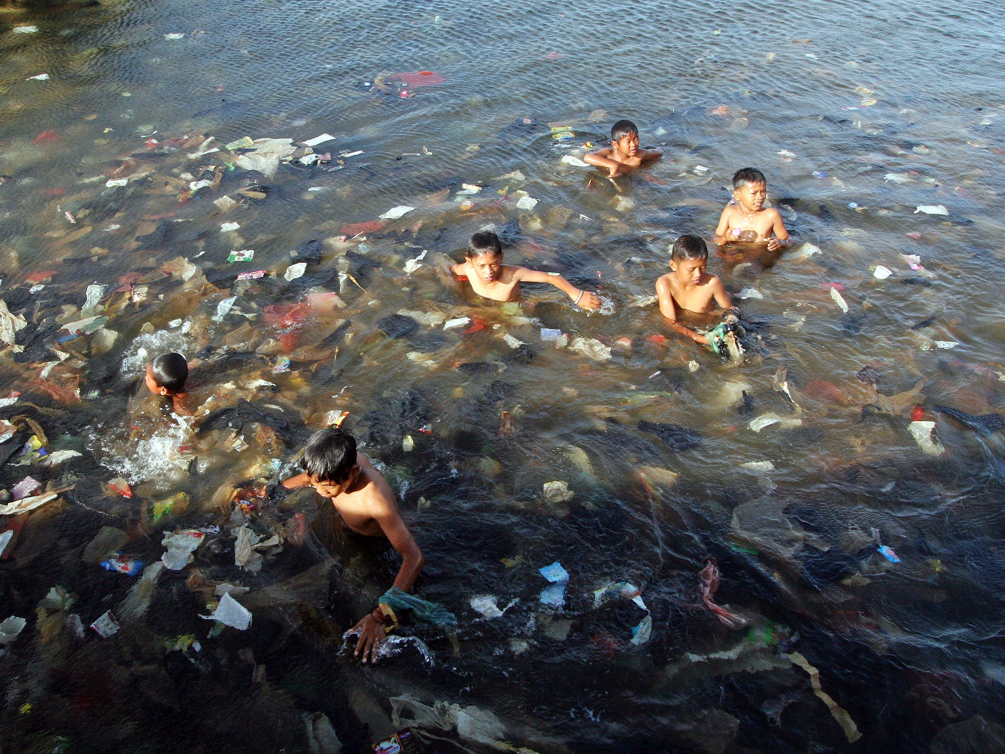 Plastic is polluting the world’s oceans: children swim in a sea full of garbage in North Jakarta, Indonesia