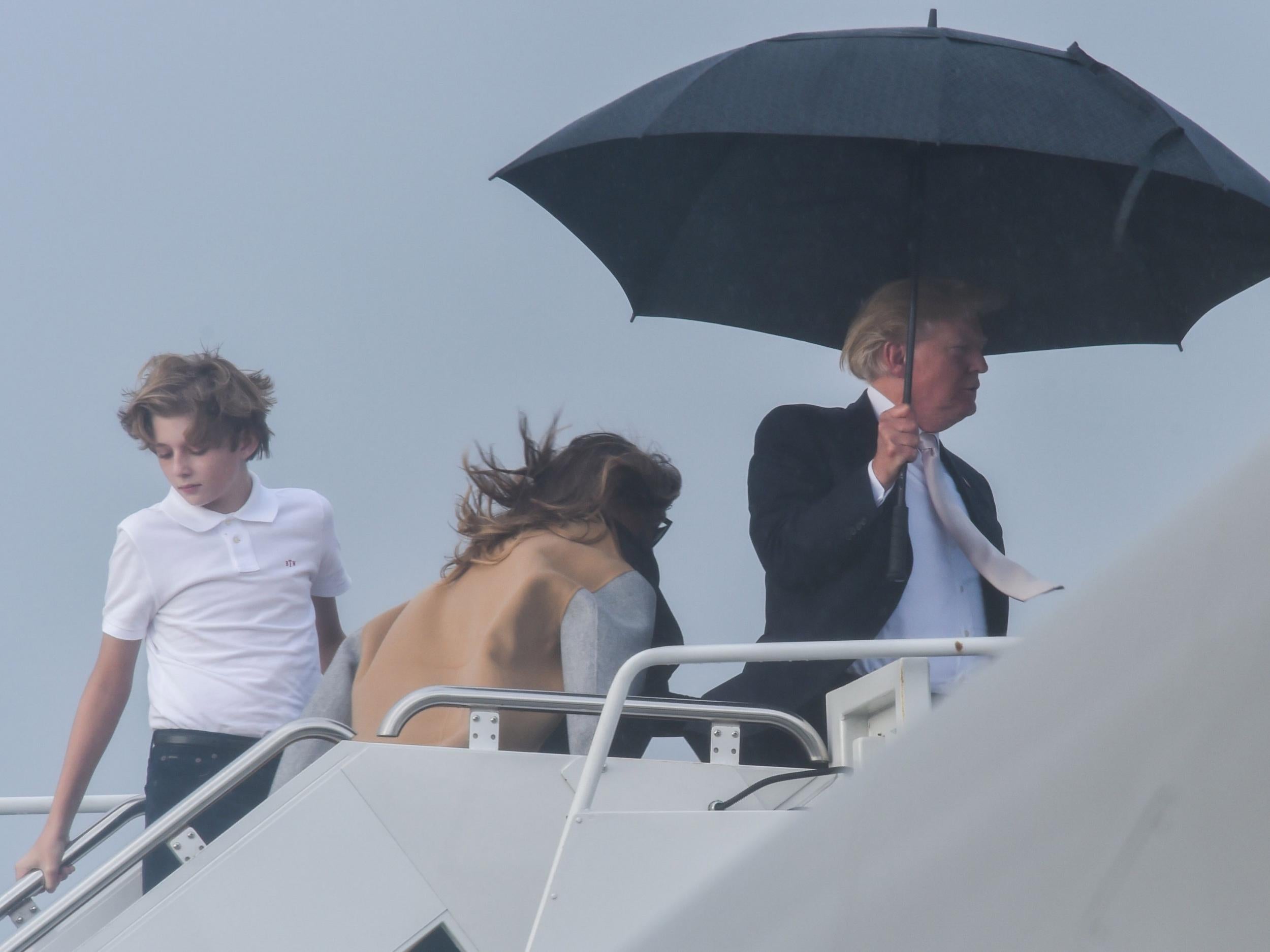 US President Donald Trump holds an umbrella as he waits for his son Barron and wife Melania to board Air Force One at Palm Beach International Airport in West Palm Beach, Florida