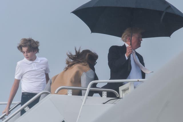 US President Donald Trump holds an umbrella as he waits for his son Barron and wife Melania to board Air Force One at Palm Beach International Airport in West Palm Beach, Florida