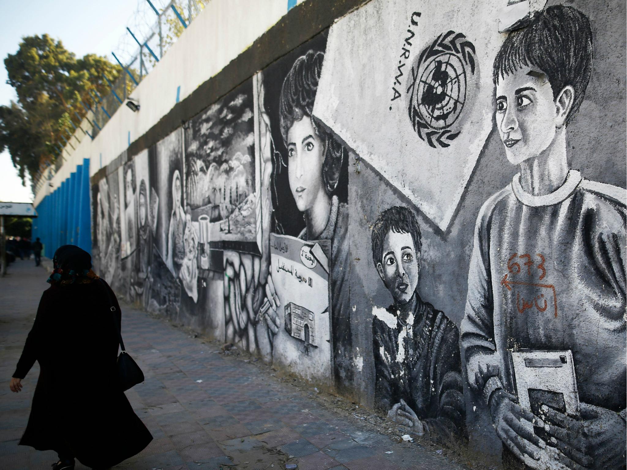 A Palestinian woman walks past graffiti painted on the wall of the building of the UNRWA headquarters in Gaza City on 8 January 2018.