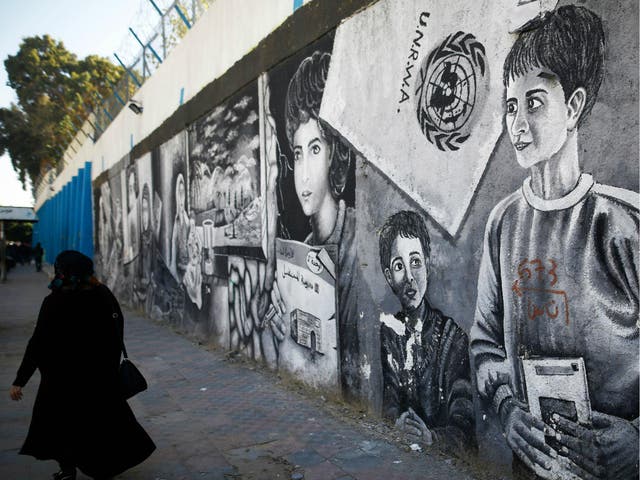 A Palestinian women walks past graffiti painted on the wall of the building of the UNRWA headquarters in Gaza City on 8 January 2018.