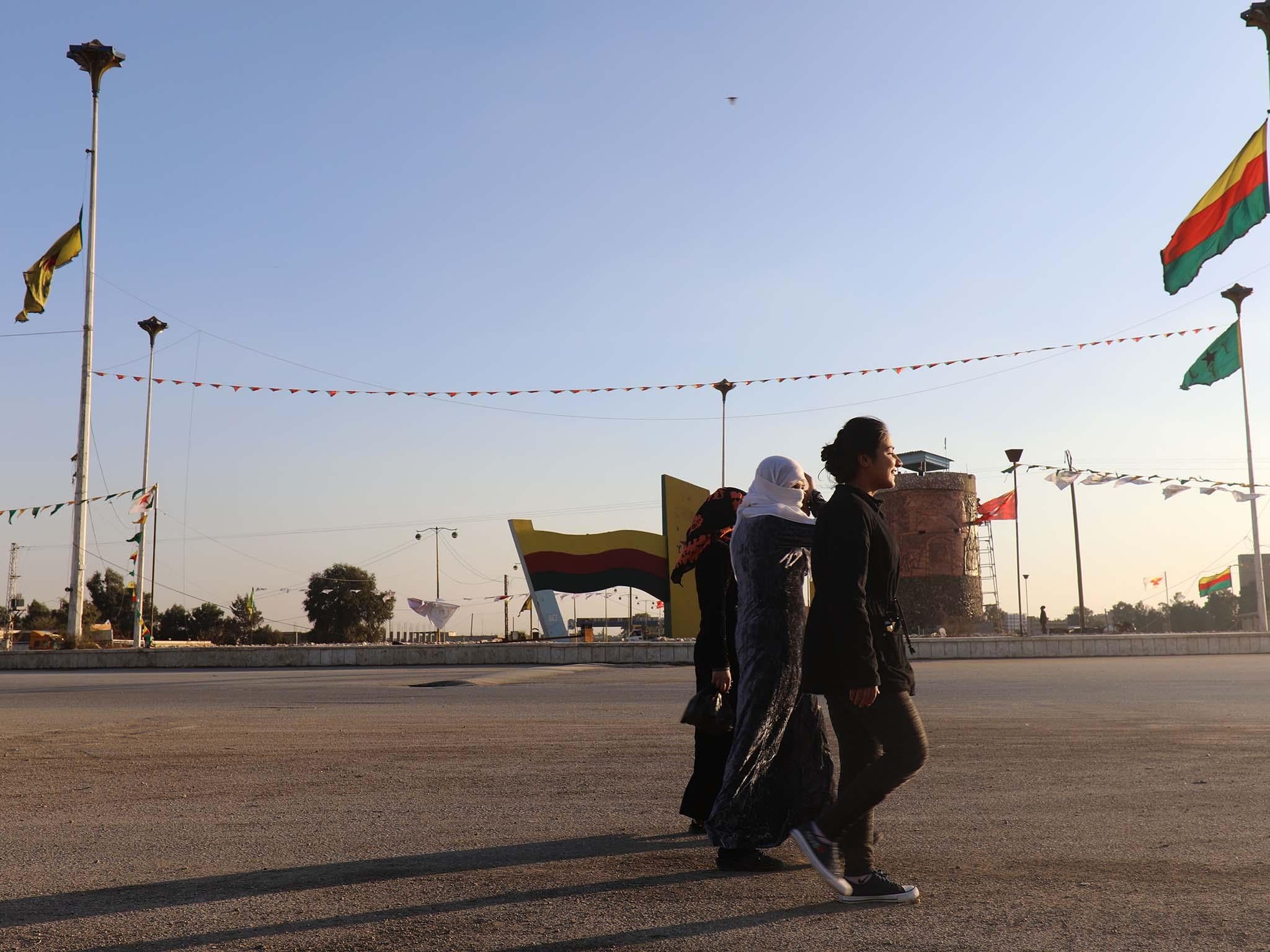 Syrian Women walk in a street next to Kurdish flags in the Syrian town of Hasakah, in northern Syria, on 30 November 2017