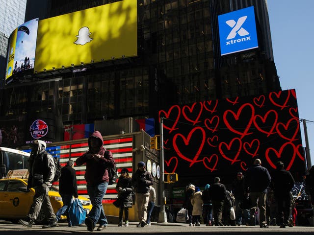 Pedestrians cross the street below a billboard displaying the logo of Snapchat above Times Square in New York March 12, 2015