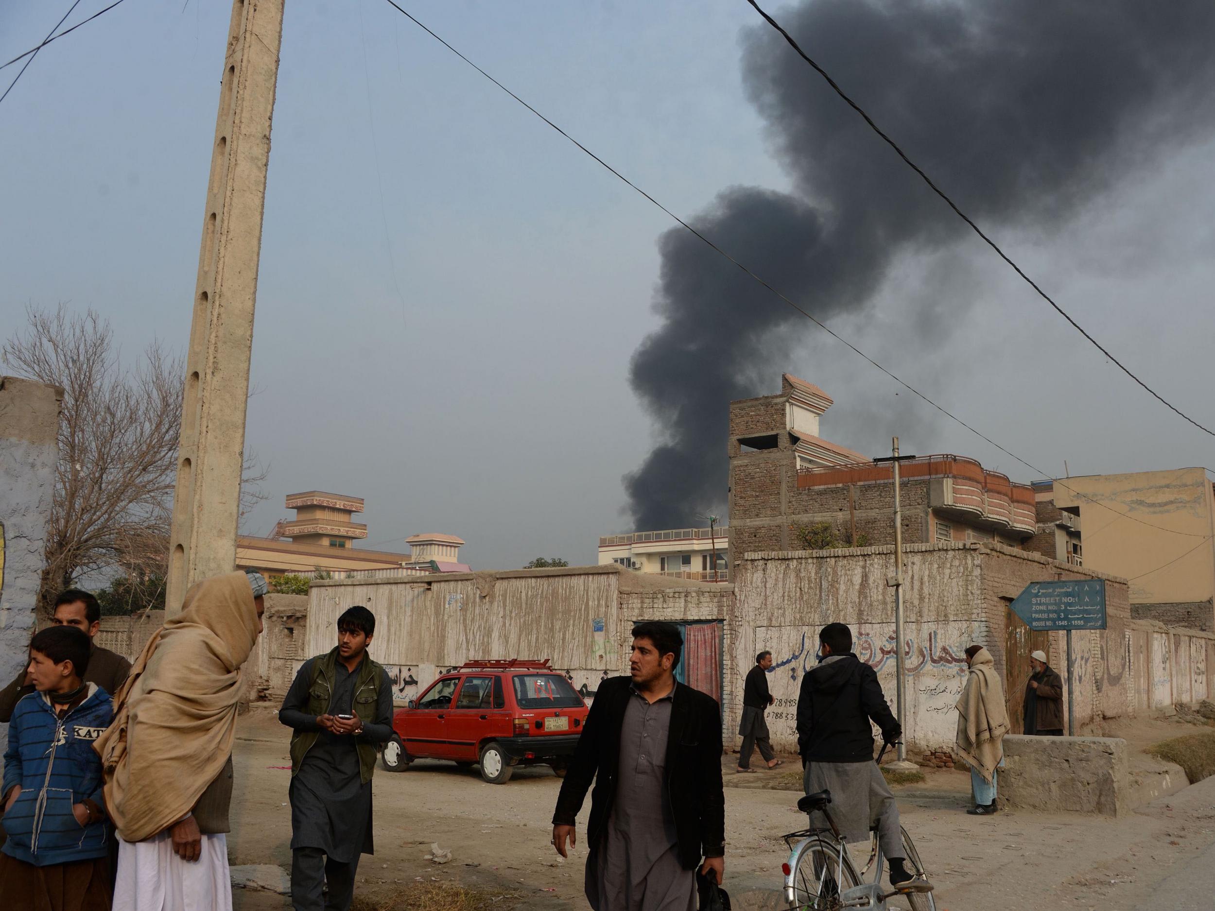 Afghan civilians gather on a street next to a plume of smoke coming from the area around an office of the British charity Save the Children during an ongoing attack in Jalalabad on 24 January 2018