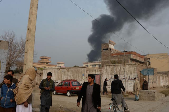 Afghan civilians gather on a street next to a plume of smoke coming from the area around an office of the British charity Save the Children during an ongoing attack in Jalalabad on 24 January 2018