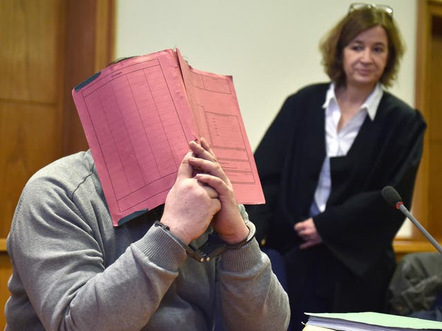 Niels Hoegel hiding his face behind a folder as he waits next to his lawyer
