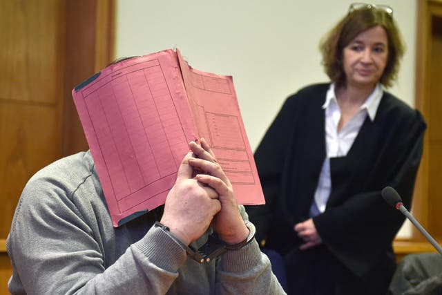Niels Hoegel hiding his face behind a folder as he waits next to his lawyer