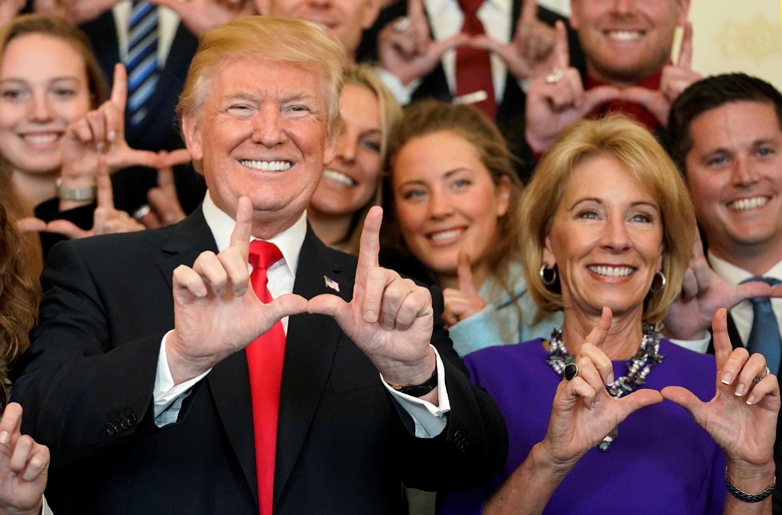 President Donald Trump and Education Secretary Betsy DeVos make "U" symbols with their hands while posing with the Utah Skiing team