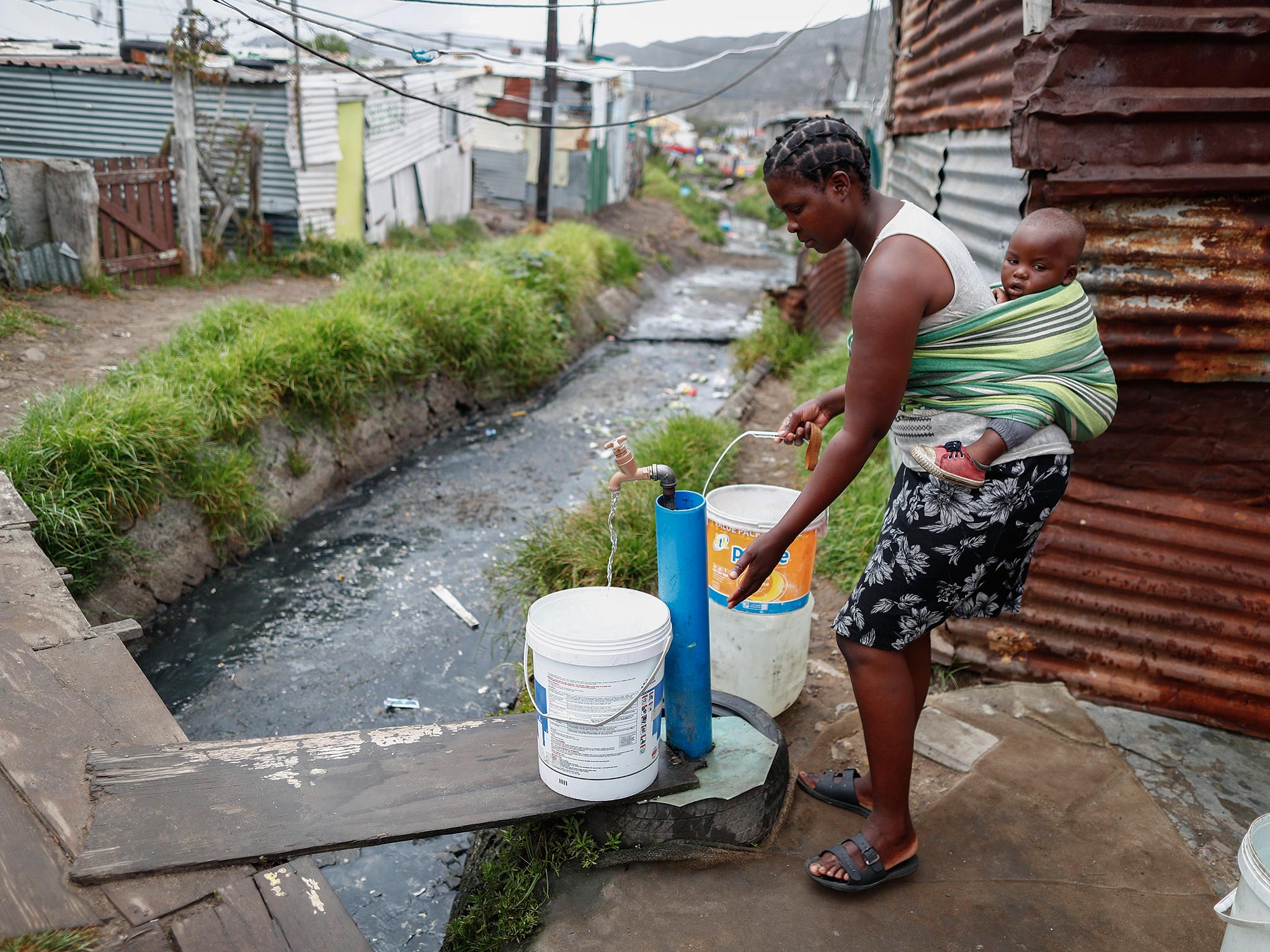 A resident collects drinking water from a communal municipal tap in Cape Town, South Africa