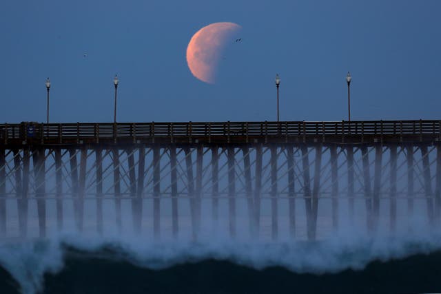 A blue moon comes out of a lunar eclipse as it sets past an ocean pier in Oceanside, California