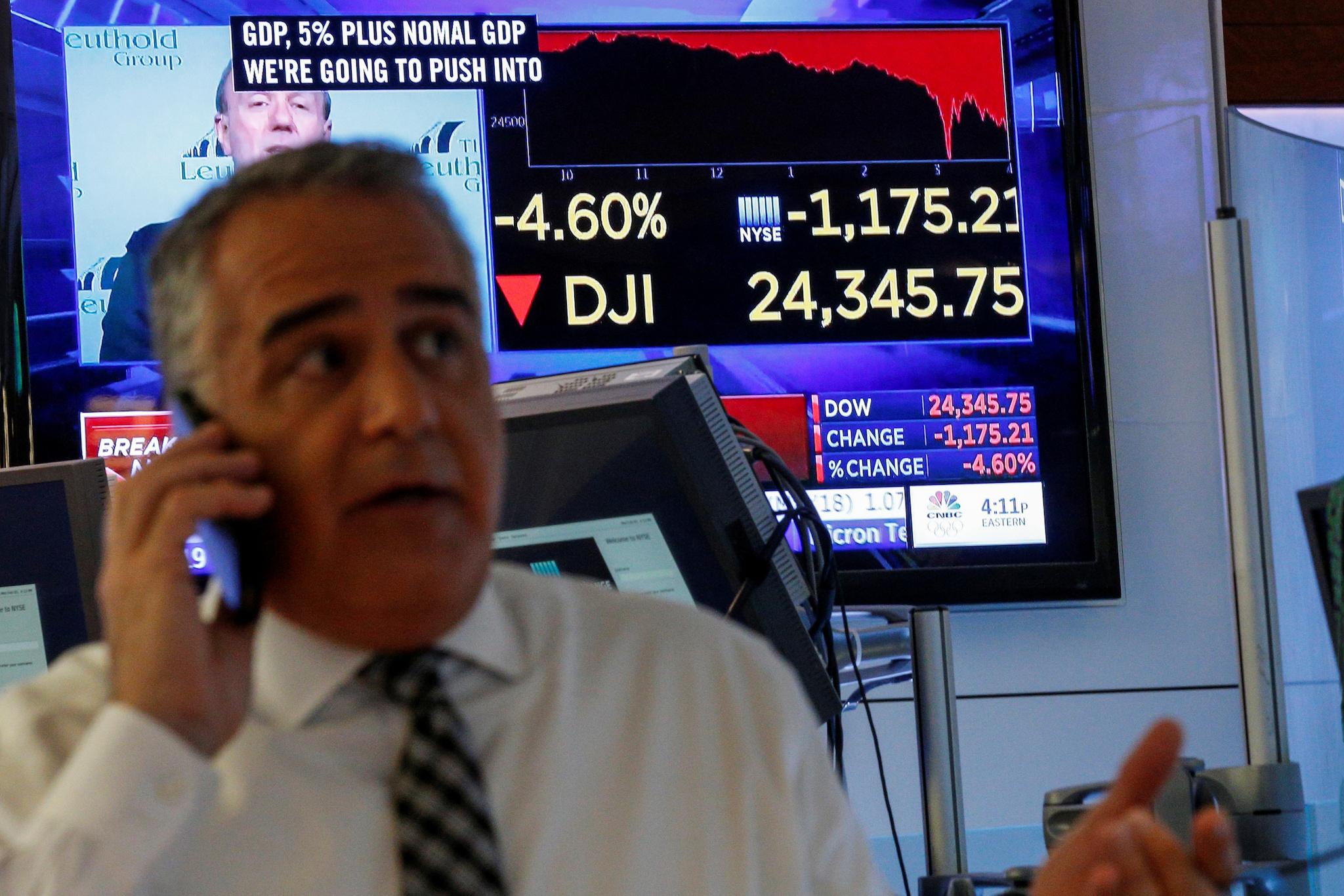 A trader works on the floor following the closing bell as a screen shows the Dow Jones Industrial Average on the New York Stock Exchange
