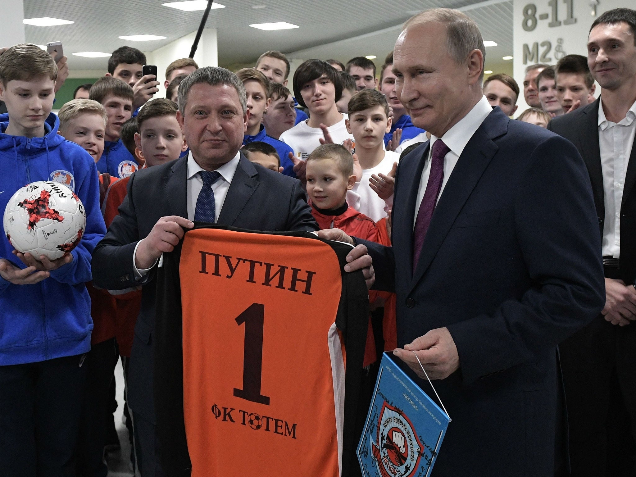 Russian President Vladimir Putin, right, holds a T-shirt with his name as he and General Director Sergei Gorbunov, second left, pose for a photo with FC Totem football team's players in Krasnoyarsk