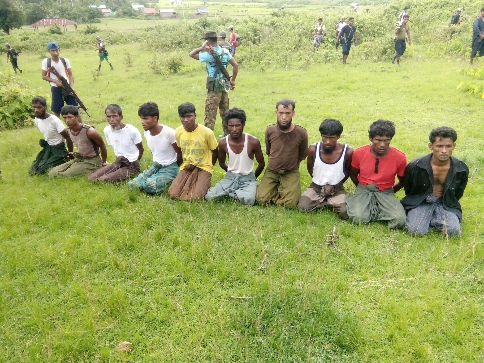 Rohingya Muslim men with their hands bound kneel as members of the Myanmar security forces stand guard at Inn Din village