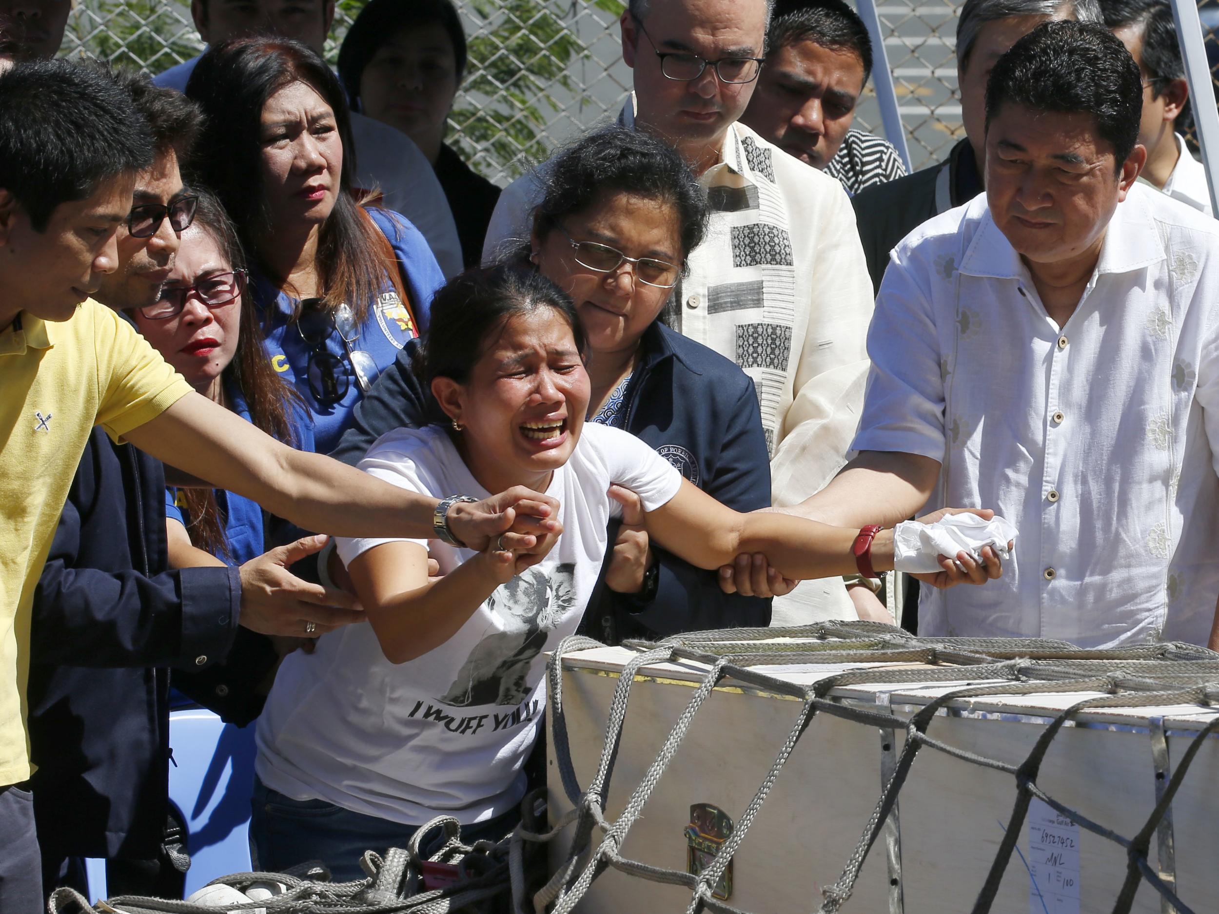 Jessica, centre, and Jojit Demafelis, left, siblings of Joanna Demafelis react as the wooden casket of her remains arrives at the Ninoy Aquino International Airport