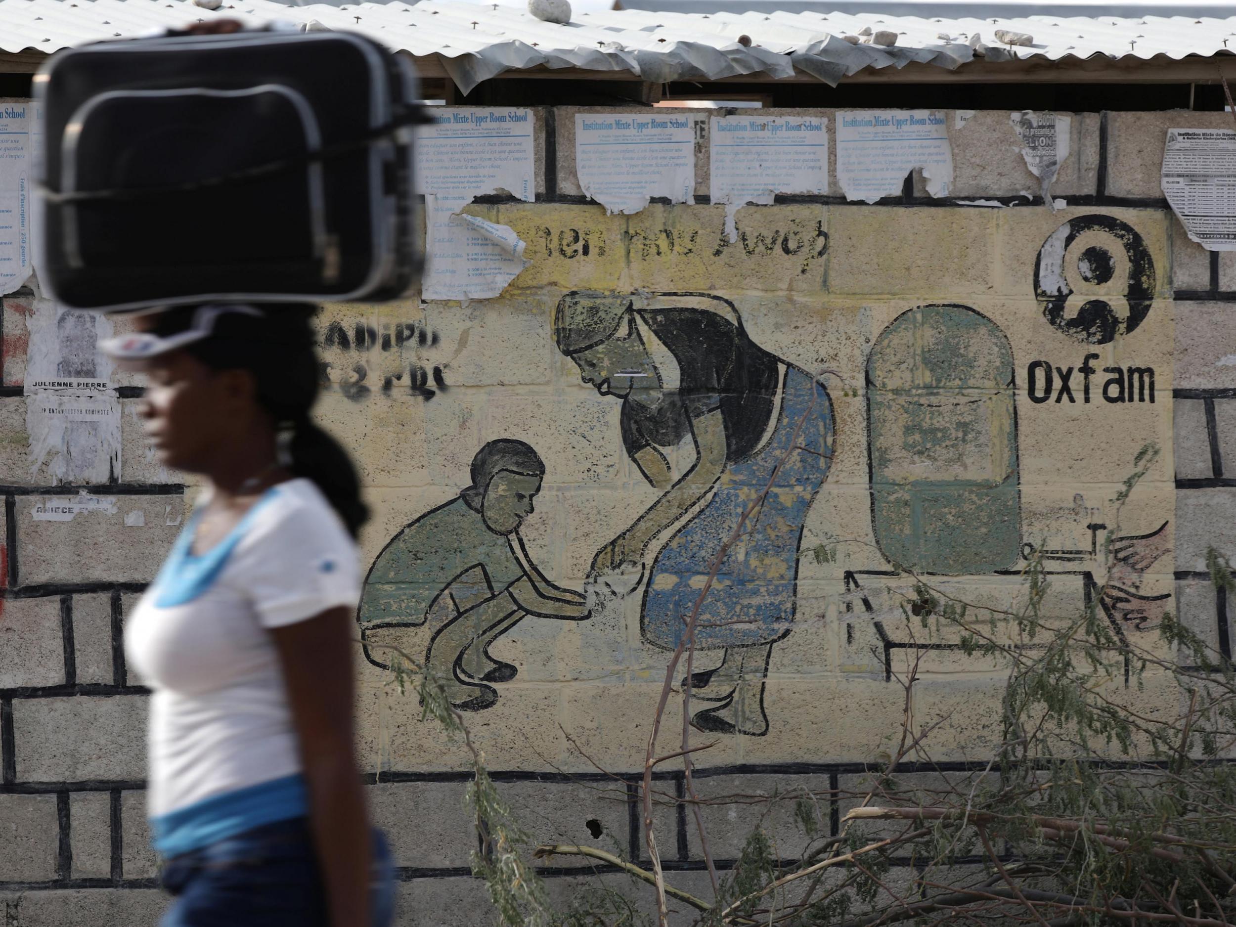 A woman walks carrying a suitcase on her head next to an Oxfam sign in Corail, a camp for displaced people of the 2010 earthquake, on the outskirts of Port-au-Prince, Haiti