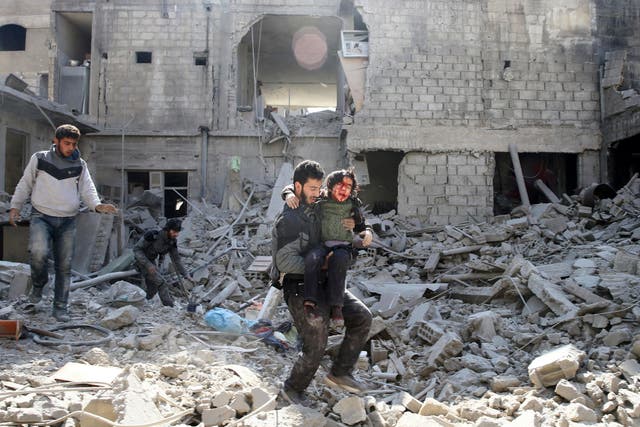 A man carries an injured boy as he walks on rubble of damaged buildings in the rebel held besieged town of Hamouriyeh, eastern Ghouta