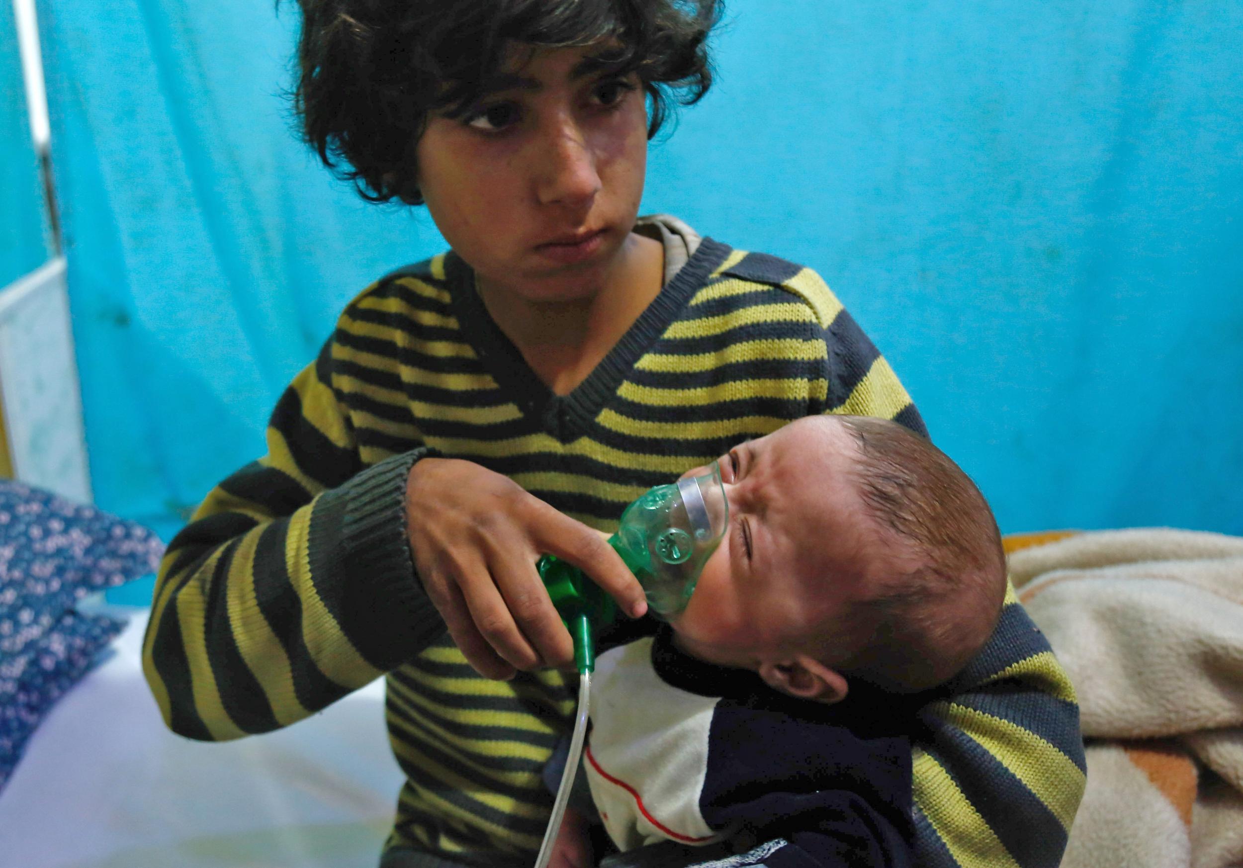 A Syrian boy holds an oxygen mask over the face of an infant at a make-shift hospital following a reported gas attack on the rebel-held besieged town of Douma in eastern Ghouta on 22 January 22 2018