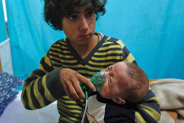 A Syrian boy holds an oxygen mask over the face of an infant at a make-shift hospital following a reported gas attack on the rebel-held besieged town of Douma in eastern Ghouta on 22 January 22 2018