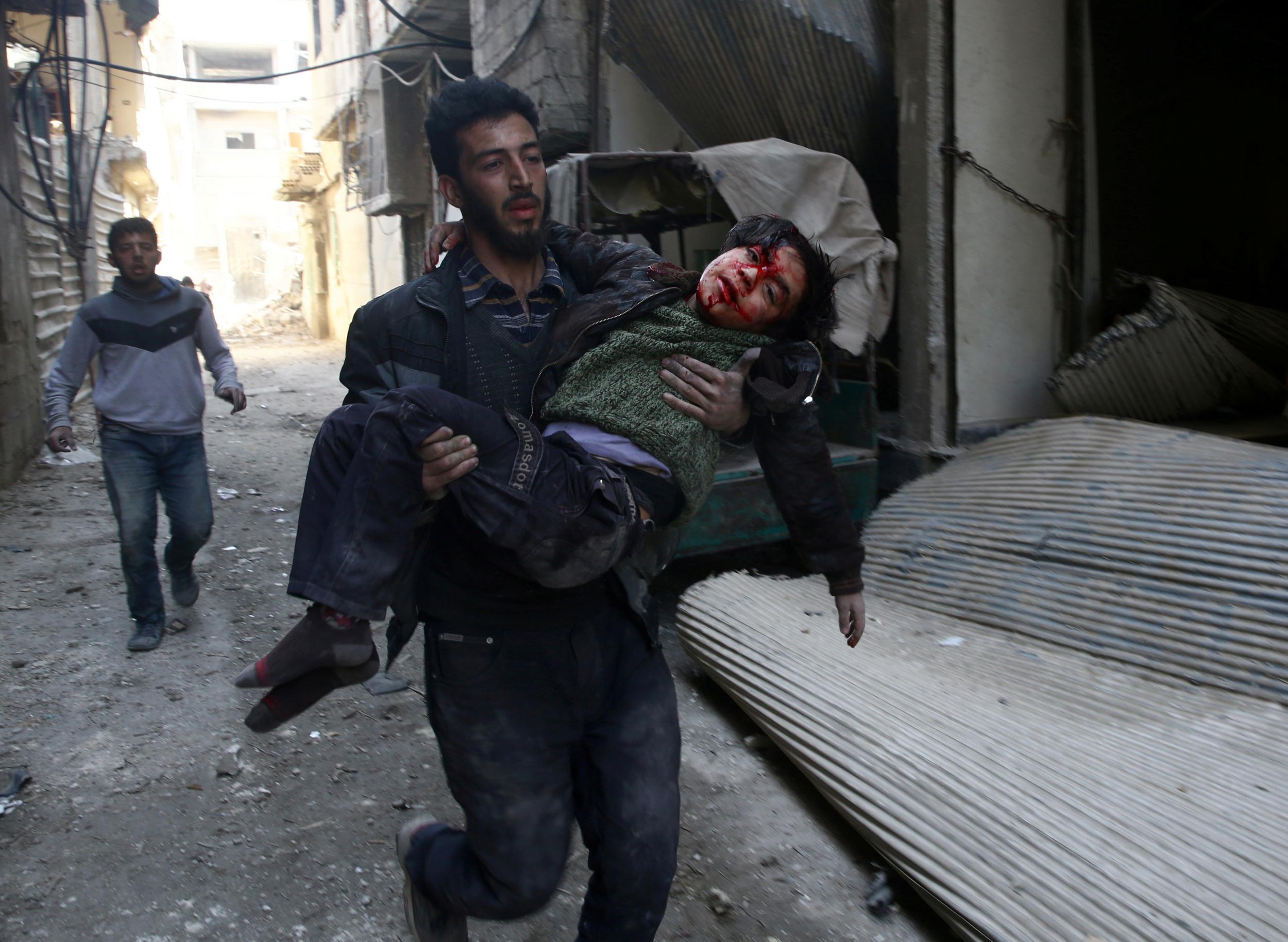 Mohammed Abu Anas runs with an injured boy in the besieged eastern Ghouta town of Hamouriyeh near Damascus, Syria, on 21 February 2018