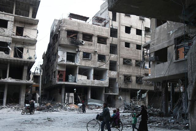 Syrians walk past destroyed buildings in Arbin in the rebel-held enclave of Eastern Ghouta on February 25, 2018
