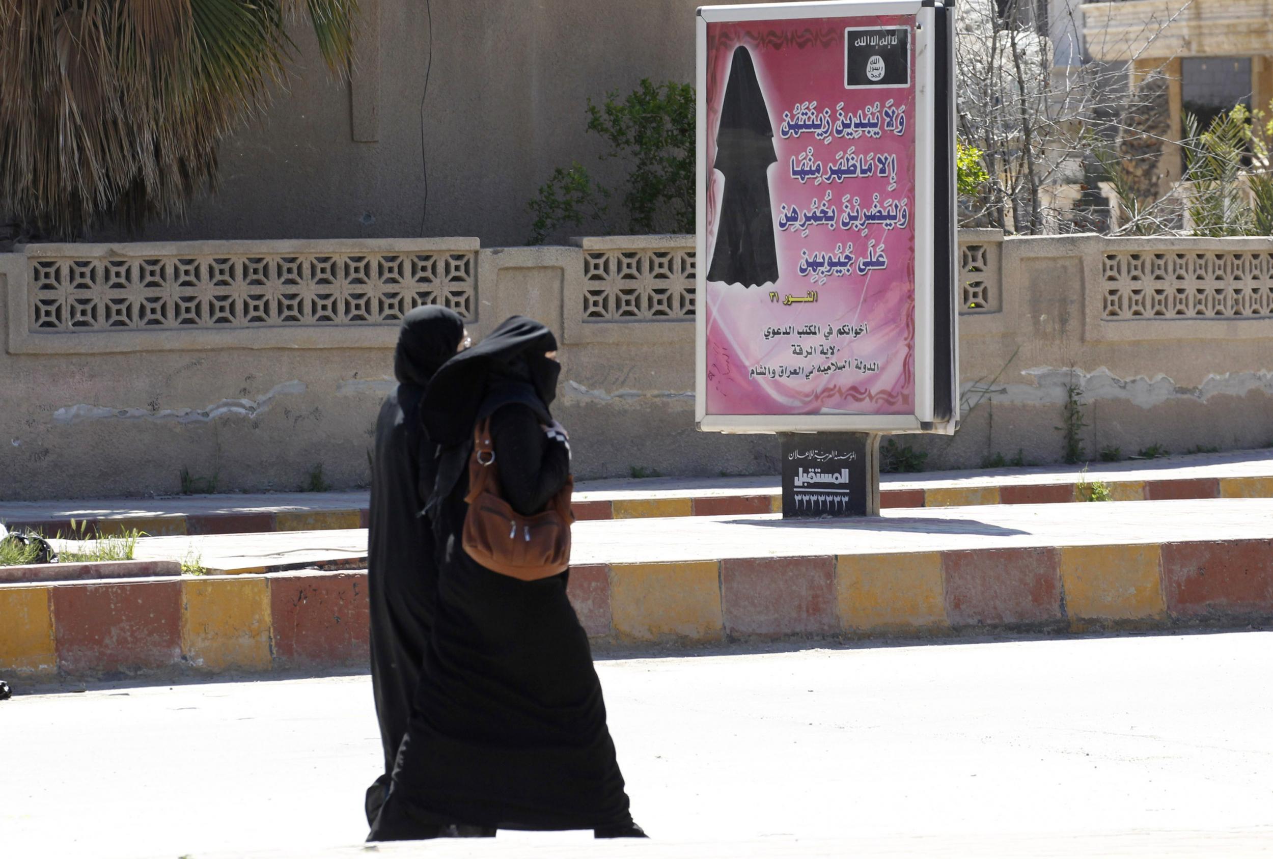 Veiled women walk past a billboard that carries a verse from the Qu'ran urging women to wear a hijab in the then Isis-controlled province of Raqqa on 31 March 2014