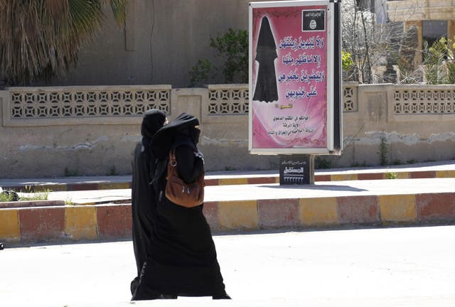 Veiled women walk past a billboard that carries a verse from the Qu'ran urging women to wear a hijab in the then Isis-controlled province of Raqqa on 31 March 2014